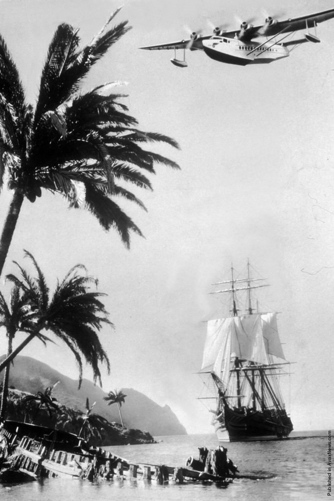 A Pan American Airways flying boat over a clipper ship on the Spanish coast, 1938.