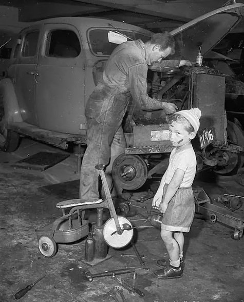 Young boy with dinky in car workshop while his father services a car, Bondi, 1955.