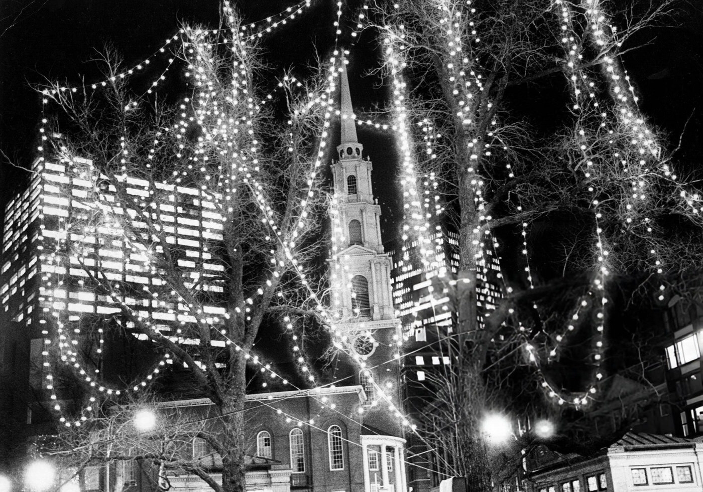 The Park Street Church is framed by Christmas lights in the trees on Boston Common, 1974.