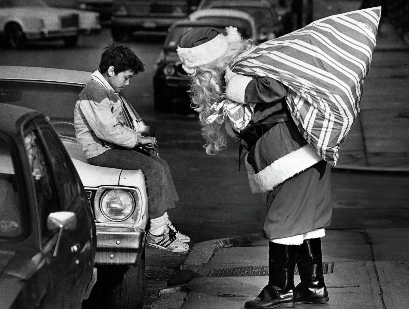 Santa Claus stops to inspect a cut on a boy's finger while delivering presents for homeless children in Boston, 1985.