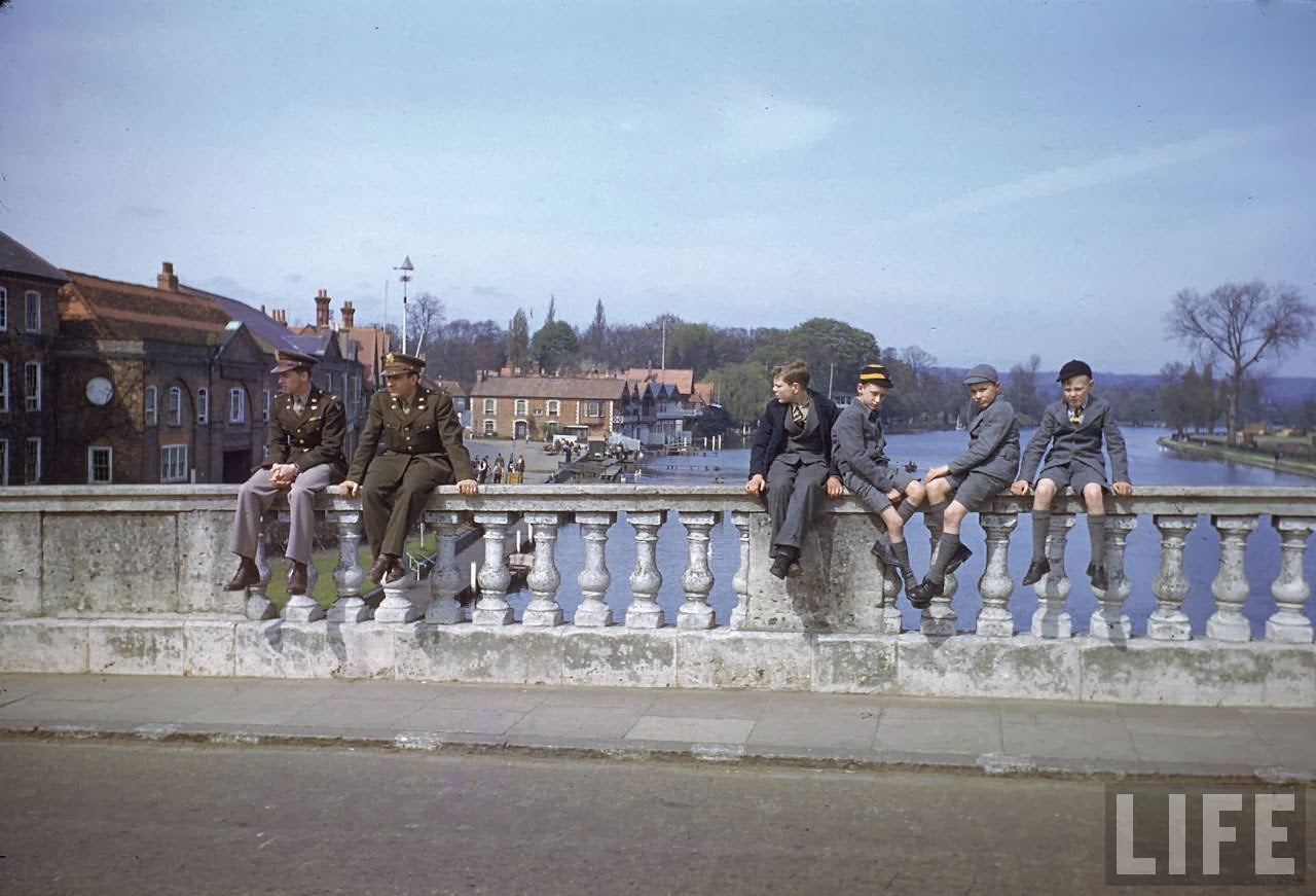 American soldiers and a group of English school children sitting on bridge over the Thames River.