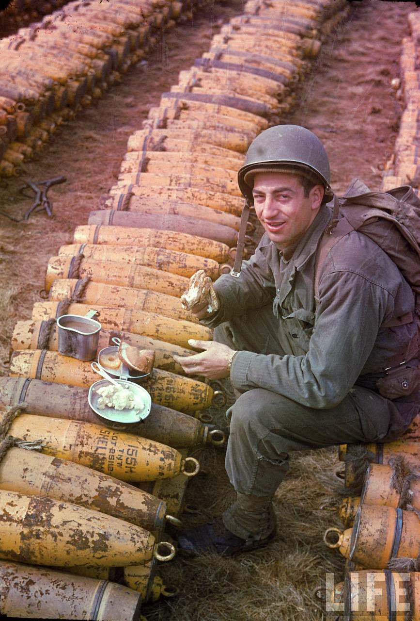 American soldier eating his dinner atop ammunition stockpiled for the impending D-Day invasion of France.