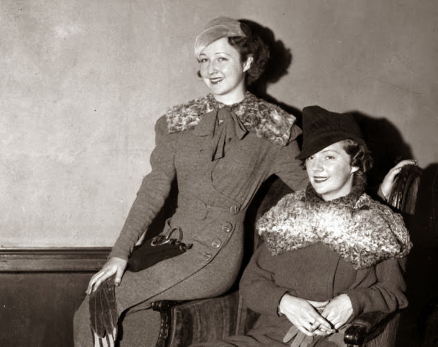 Model Mona Mora (l.) wears a gray woolen coat dress with a removable sailor collar, and Lee Sherman (r.) wears a bright green tweed fall suit with a matching gray krimmer fur high crown fabric hat at a 1933 fashion show at Hotel Pennsylvania.