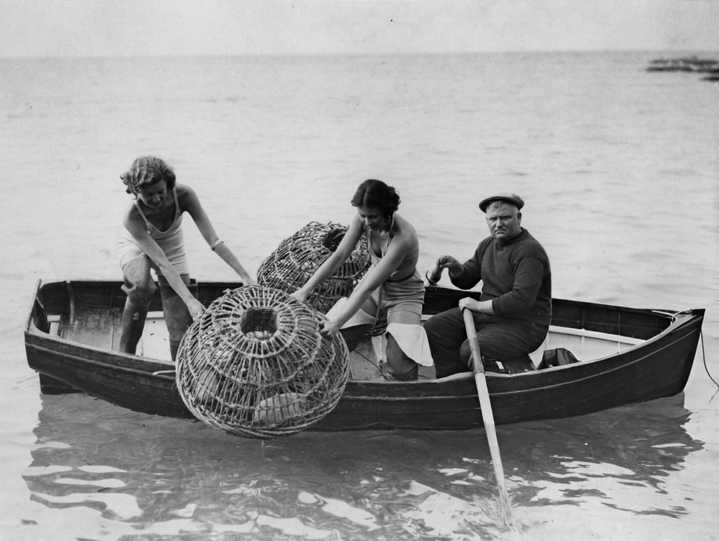 Two holidaymaking girls help a fisherman with his lobster catch, 1934.