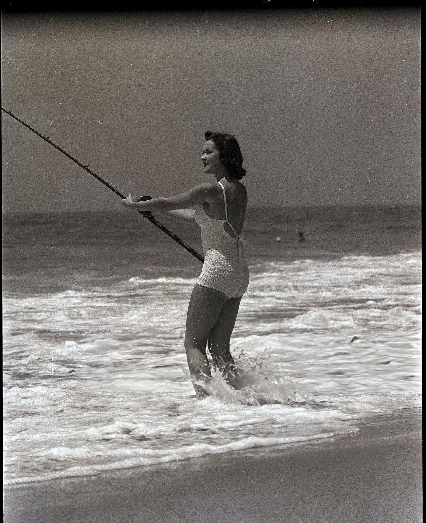 Norma Ellis stands in the surf fishing, 1950.