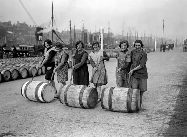 Yarmouth fisher-girls push barrels of herring along the quayside using long poles, 1929.