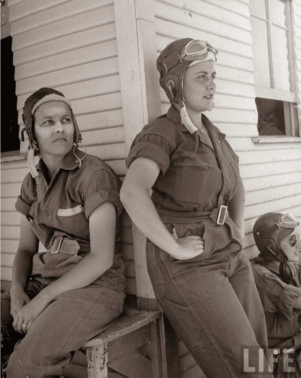Rebecca Edwards, 22, w. cream on her sunburned face & Lorena Daly, both pilot trainees in the Women's Flying Training Detachment, sporting goggled leather helmets & G.I. coveralls as they lean against primary hangar fr. which they fly, at Avenger Field.