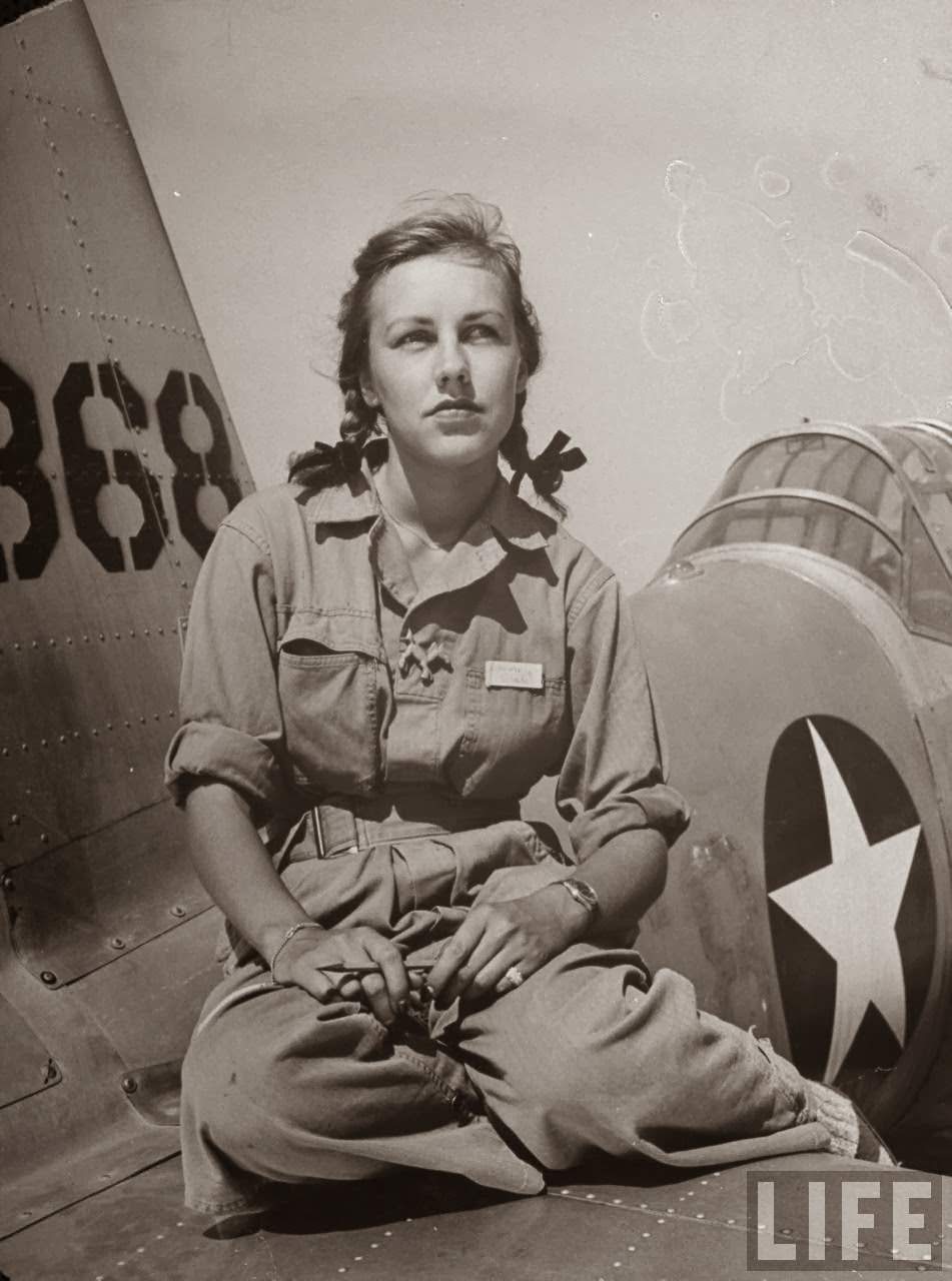 Shirley Slade, pilot trainee in Women's Fllying Training Detachment, sporting pigtails & GI coveralls as she sits on wing of her Army trainer at Avenger Field.