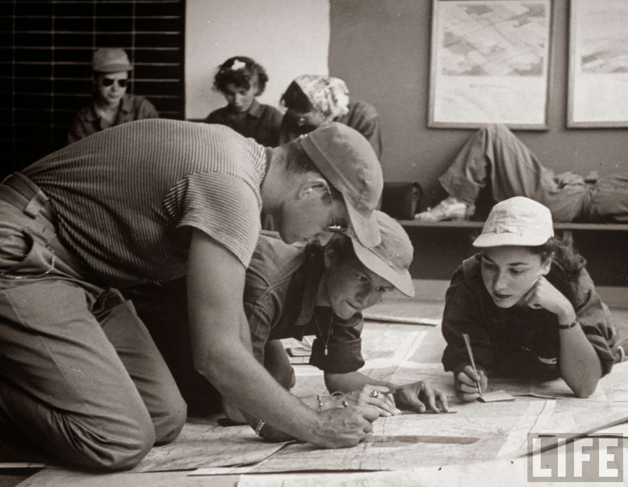 Janet Zuchowski (C) & Alice Jean May, (R) pilot trainees in Women's Fllying Training Detachment, on floor ploting cross-country flight on a map w. Norman Schaeffer (L) who helps them as one of the civilian flight instructors, at Avenger Field.
