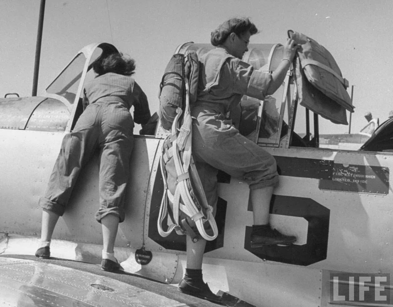 Two pilot trainees in the Women's Flying Training Detachment, climbing aboard basic trainer plane as short-legged one w. parachute places cushions in rear seat before starting instrument flight which is done in pairs, at Avenger Field.