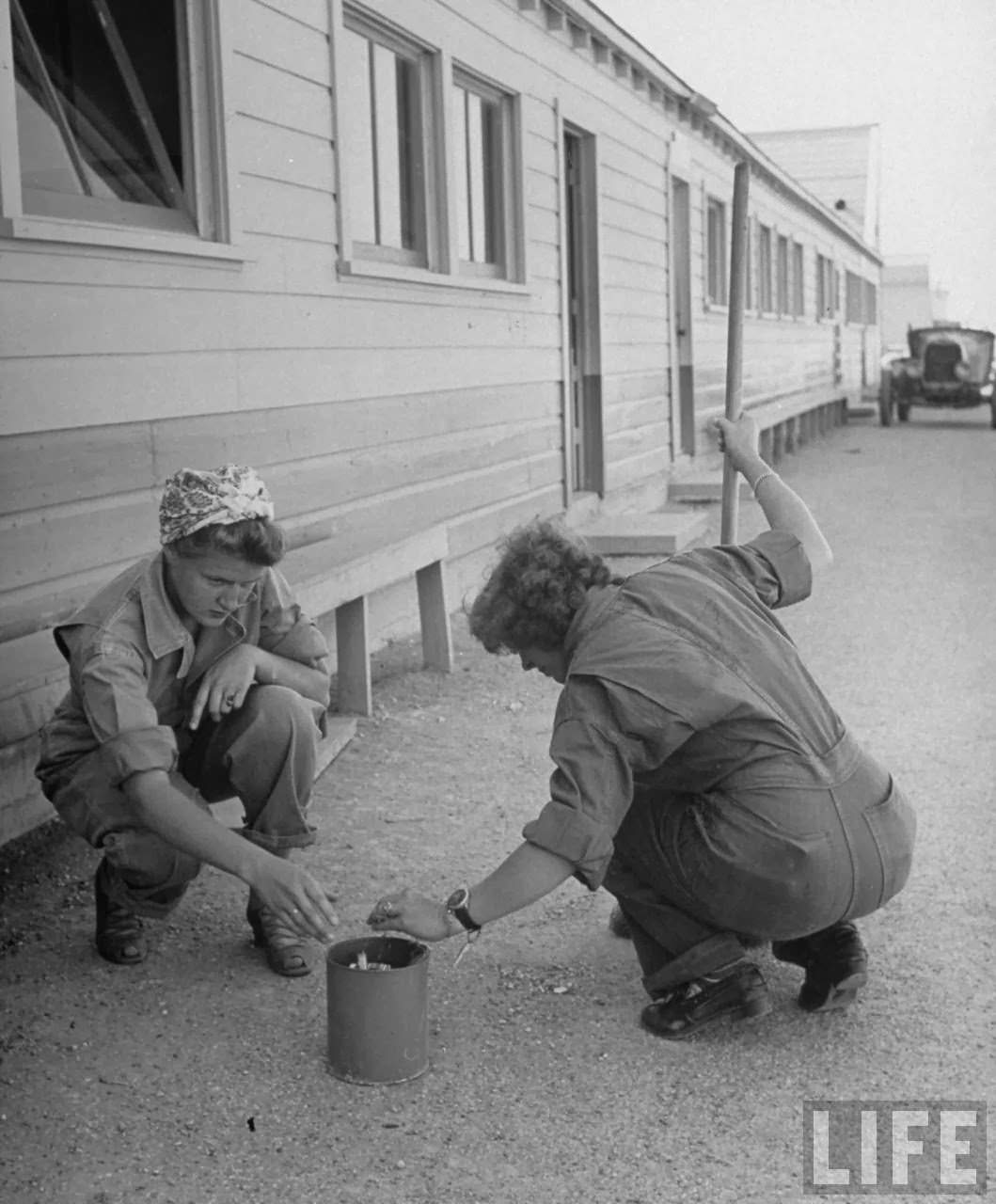 Two pilot trainees in the Women's Flying Training Detachment, policing area around barracks by picking up cigarette butts strewn around as part of their duties as "Ready Room Lieutenants," at Avenger Field.