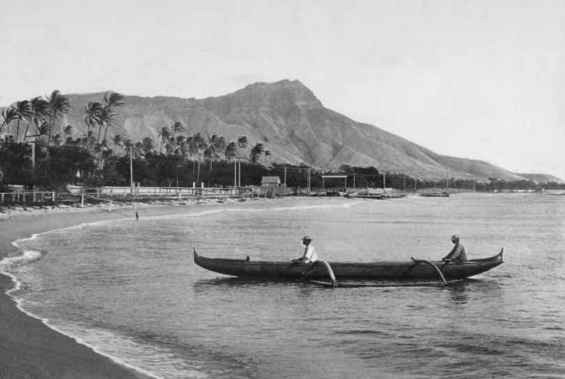 Two local men in their raft rest by the beach at Waikiki Bay with Diamond Head in the background, 1900s.