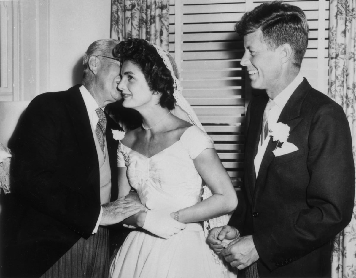 Joseph Kennedy whispers to his new daughter-in-law Jacqueline Bouvier as John F. Kennedy looks on, Newport, Rhode Island, 1953.
