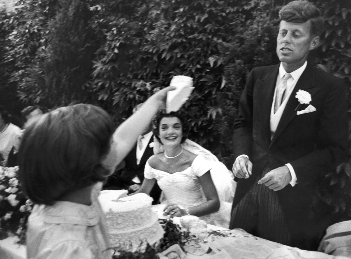 Flower girl Janet Auchincloss holds a piece of wedding cake as Jacqueline Kennedy looks on, 1953.