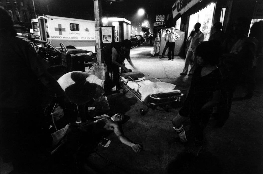 Police and ambulance arrive at the scene of a street fight; a man lies unconscious, 1979.