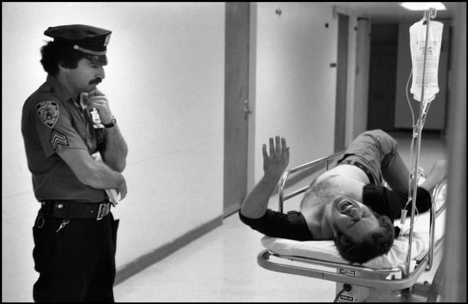 A police officer waits in the hospital waiting room for information on a leg wound victim, 1978.