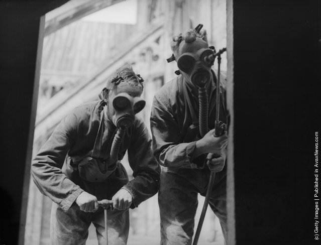 Pest control men in gas masks spraying insecticide around Winchester Cathedral, 1935.