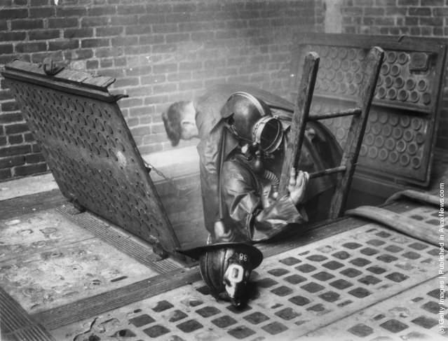 Two firefighters emerging from a smoke-filled vent, 1929.