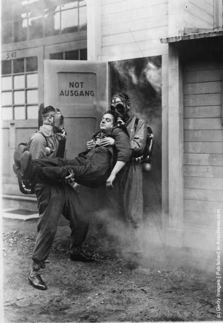 Men wearing gas masks carrying a man out of a door marked "Not Ausgang," 1935.