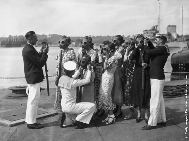 Sailors fitting gas masks on visitors at Chatham, England, during a Navy Week rehearsal, 1935.
