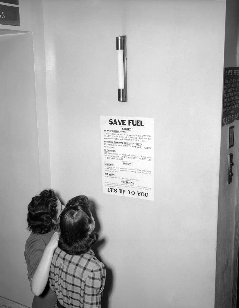 Two London office workers read the fuel economy notice displayed on every floor of the building, 1943.