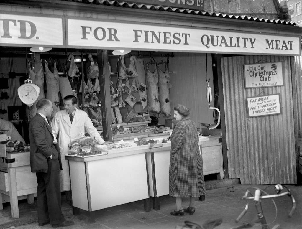 A woman studies meat in a butcher’s shop at Smithfield Market, 1954.