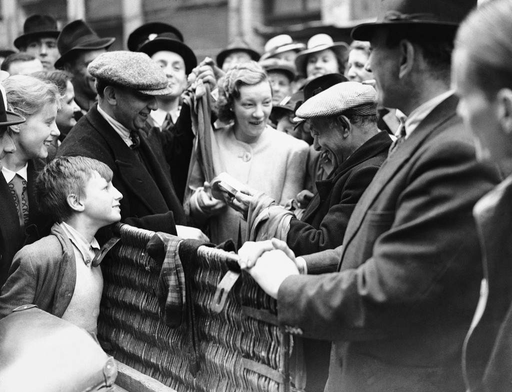 A woman makes a purchase of silk stockings at a stall in London, handing over her coupons, 1941.