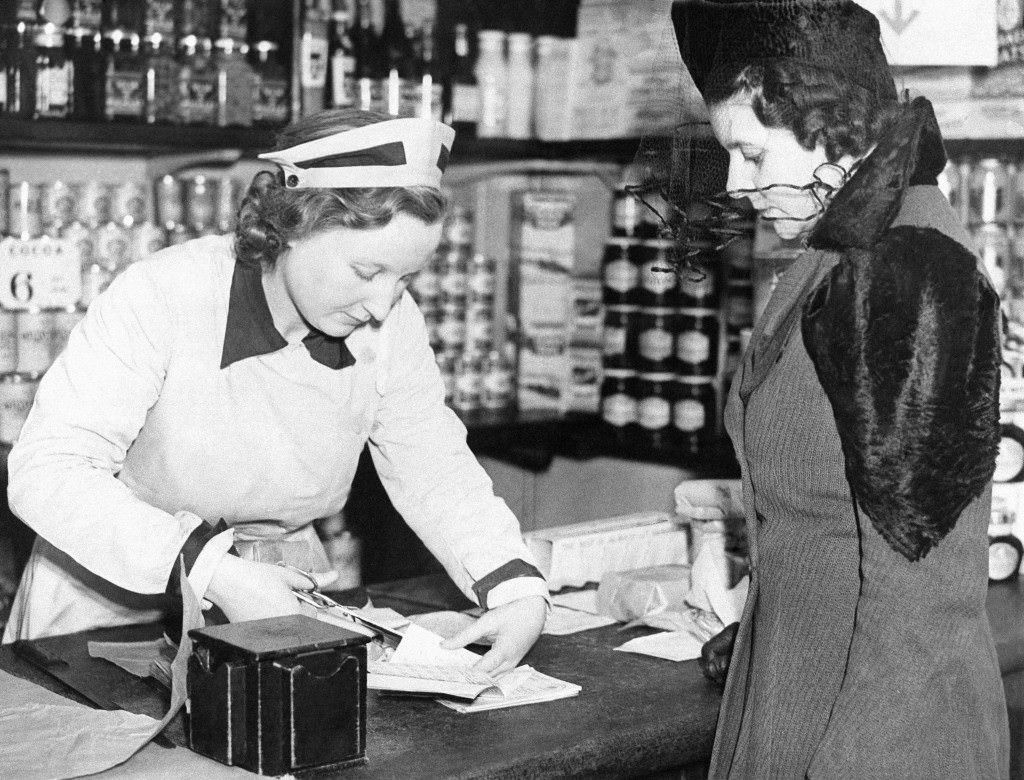 A shop assistant cuts a coupon from a London woman's ration book, 1940.