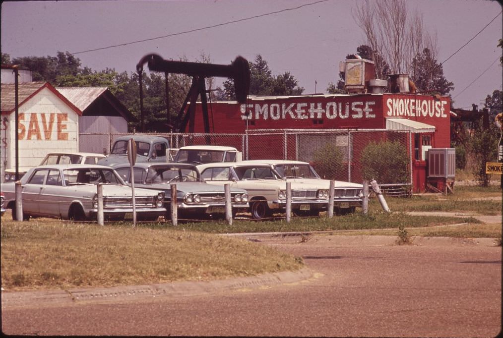An oil derrick beside a restaurant and used car lot, [Date unclear, removed].