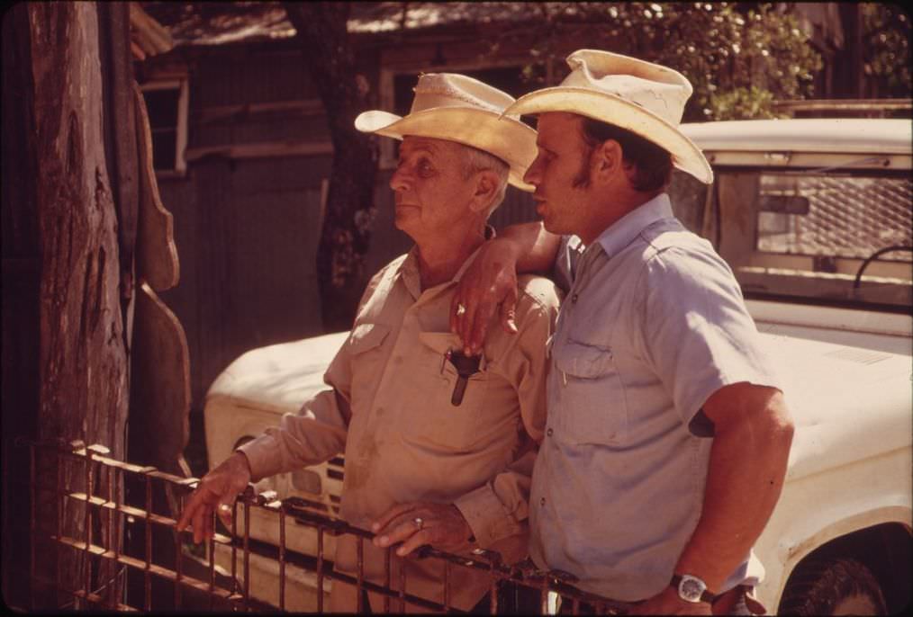 Father and son watching sheep shearing on their ranch near Leakey, Texas, 1973.