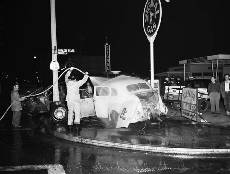 Firemen washing down cars to prevent fire at Avalon Boulevard and Manchester Avenue, Los Angeles, October 31, 1951