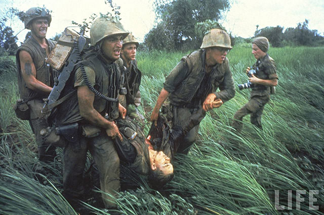 Marines recovering dead comrade while under fire during N. Vietnamese/US mil. conflict over DMZ, w. photog. Catherine LeRoy w. cameras in rear: S. Vietnam.