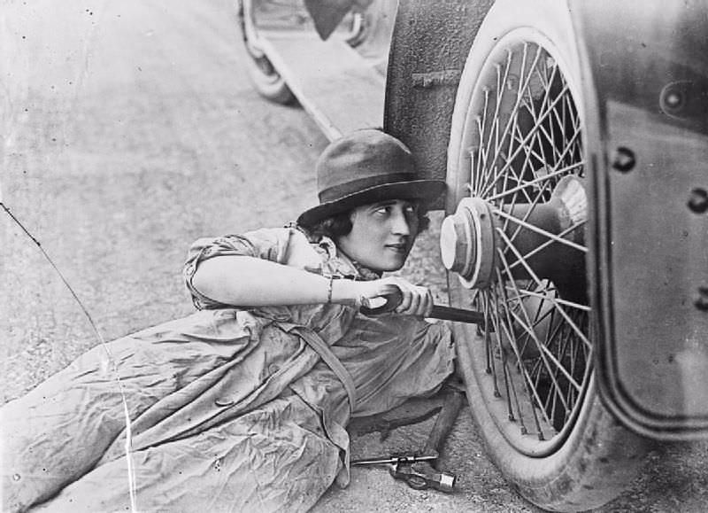 A female driver works on a wheel with a spanner during World War I.