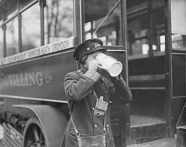 A woman bus conductor with a drink beside her bus in south London, 1916.