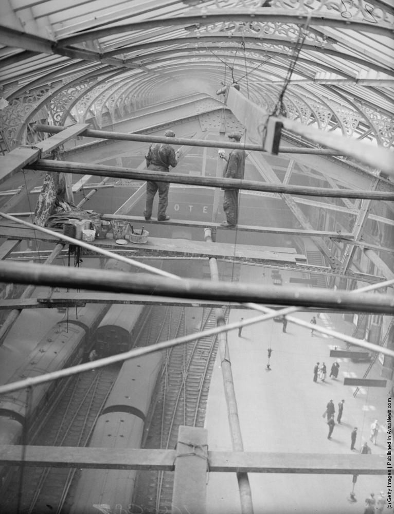 Workmen painting girders beneath the roof of Liverpool Street Station, London, 1935.