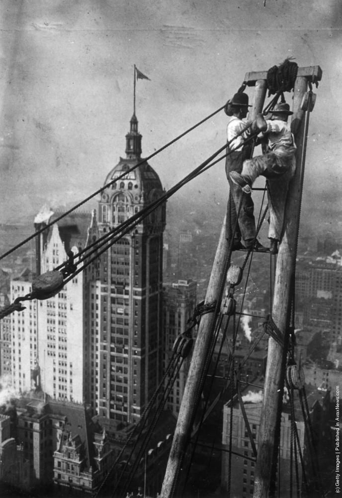 Constructions workers sitting on a hoisting ball above the New York City skyline with the Singer Building in the background, 1925.