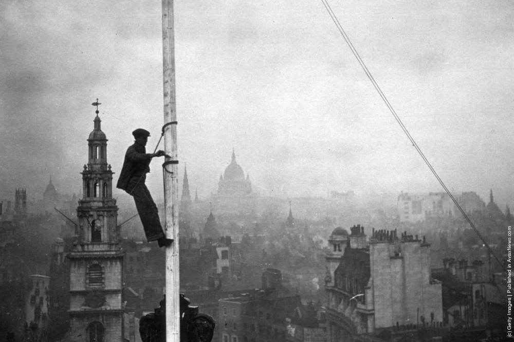 A steeplejack painting the flagstaff on Australia House, London, with St Clements Dane Church behind him, 1934.