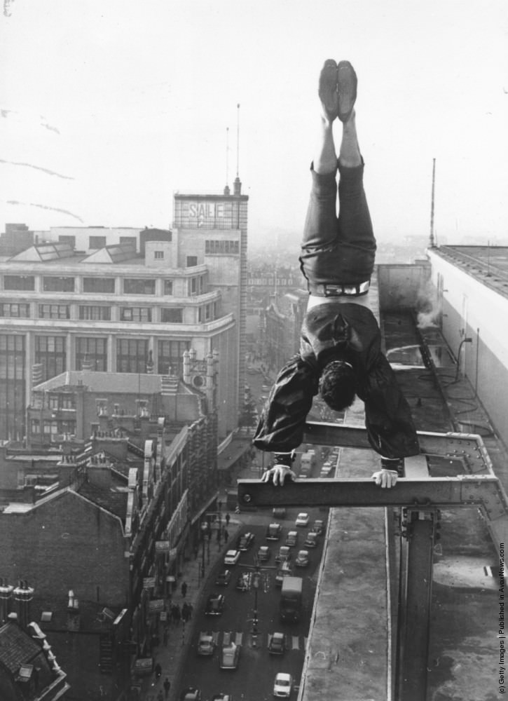 A man does a handstand on a girder high above a street in London, 1966.