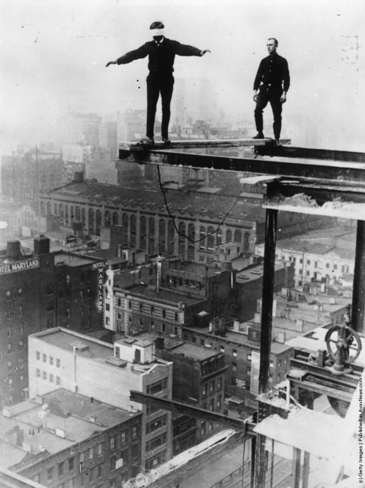 An American construction worker walking blindfolded on a construction girder twenty stories high in New York City, 1925.