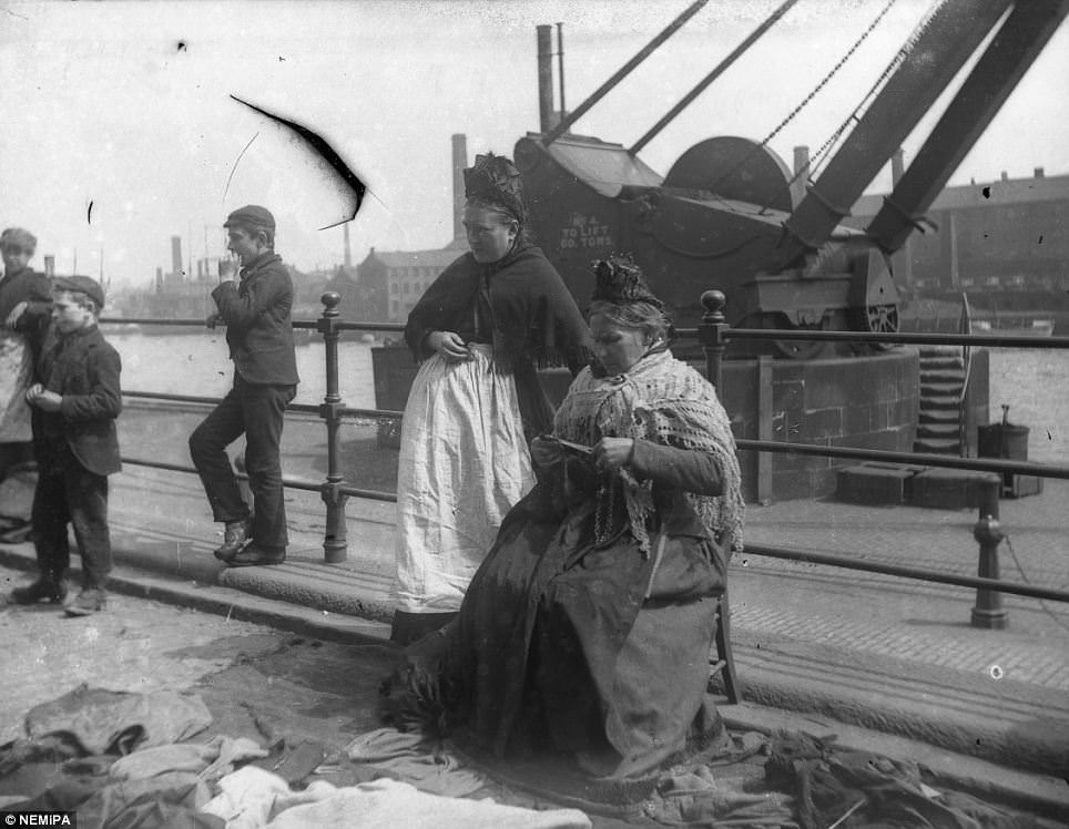 Two Newcastle matrons pass the time over some knitting by the city's Quayside, while children loiter nearby.