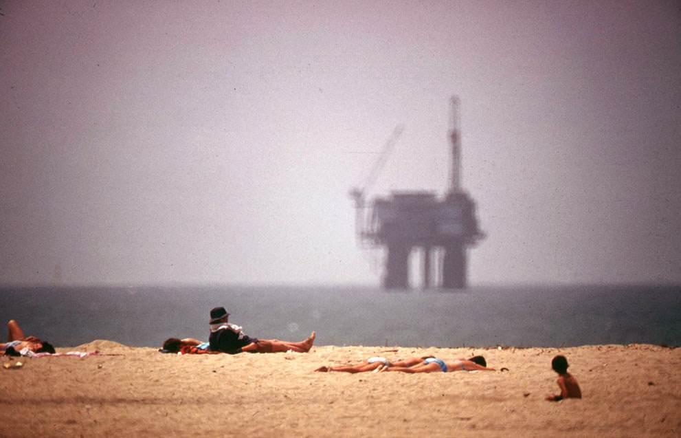 Sunbathers at Huntington Beach, California, with an oil platform visible in the distance, 1975.