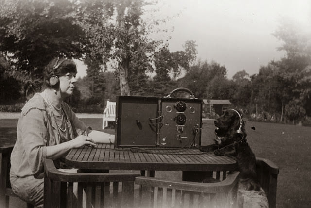 Dame Clara Butt operating a communications radio with her dog, both wearing headphones, 1930.