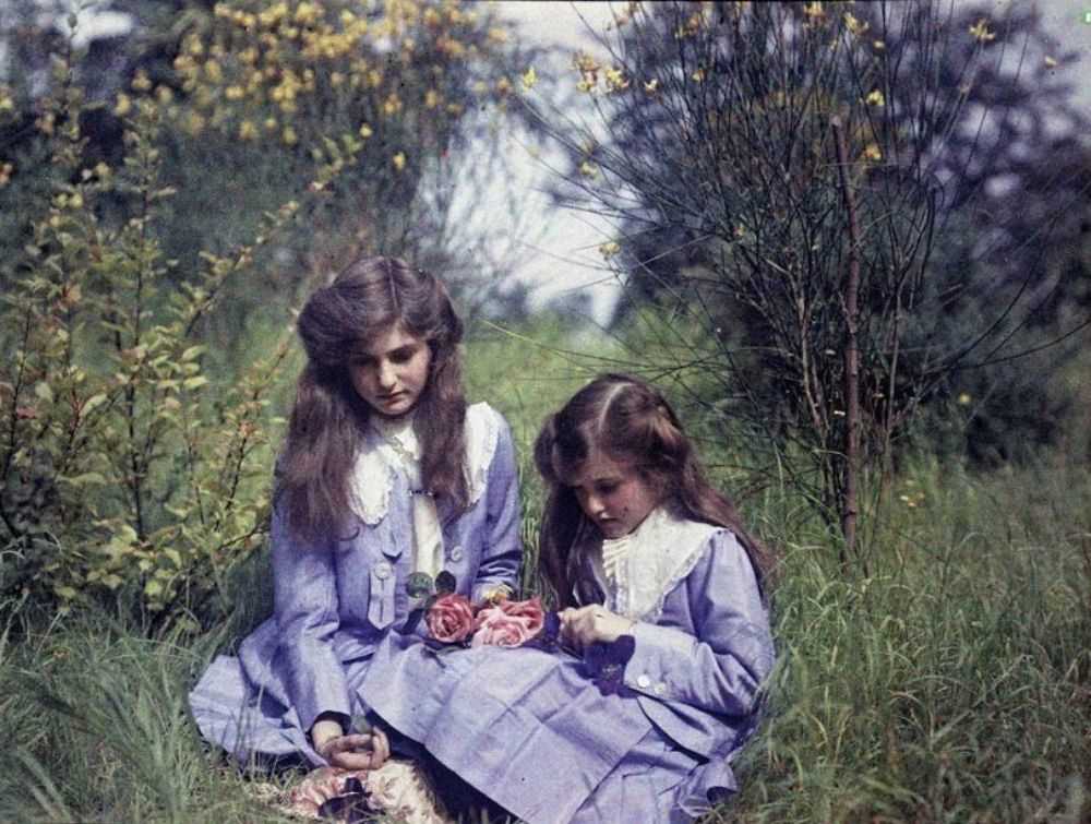 Sisters sitting in a garden tying roses together, 1911