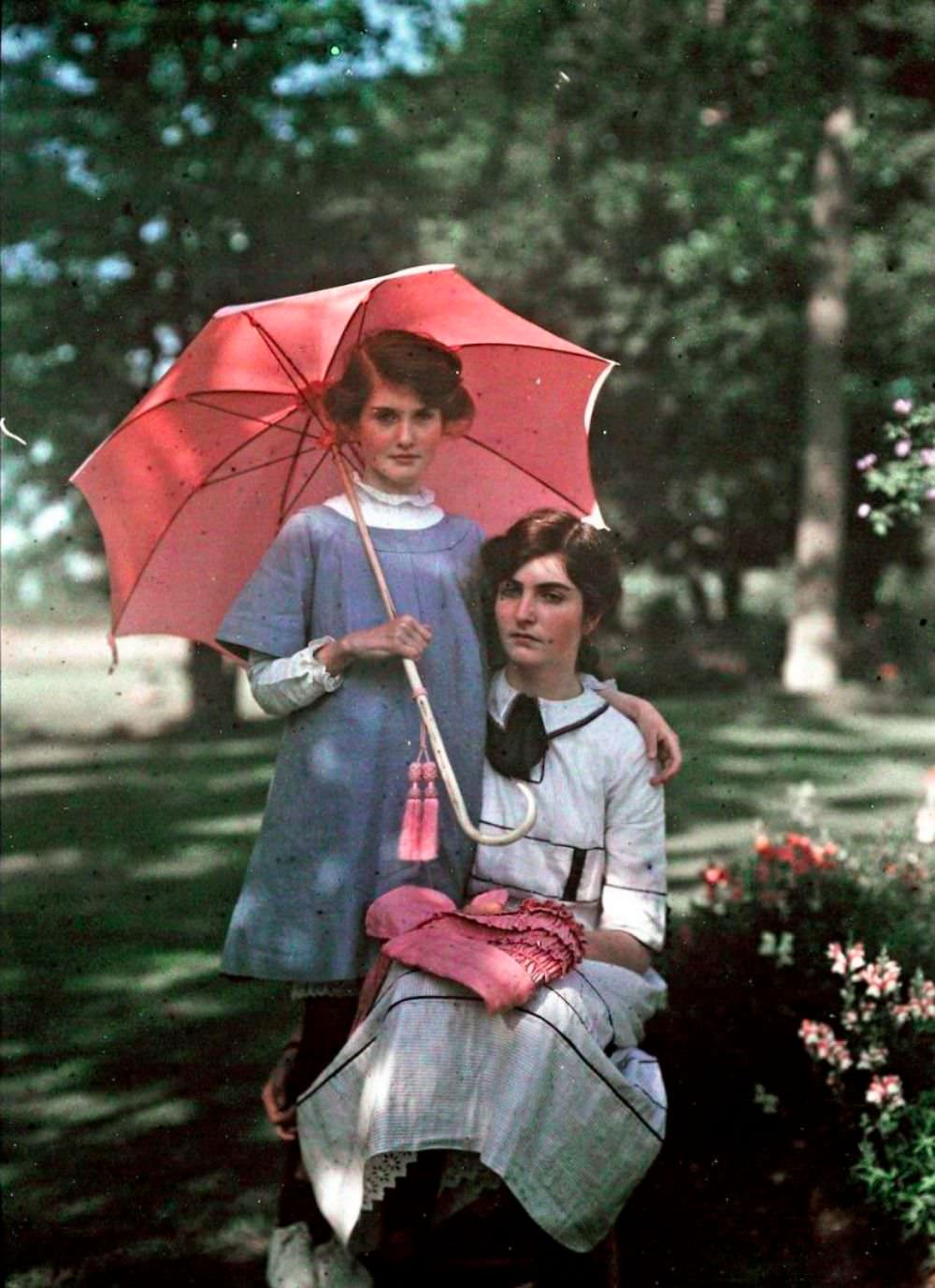 Younger girl stands beside her sister holding a pink parasol, 1908