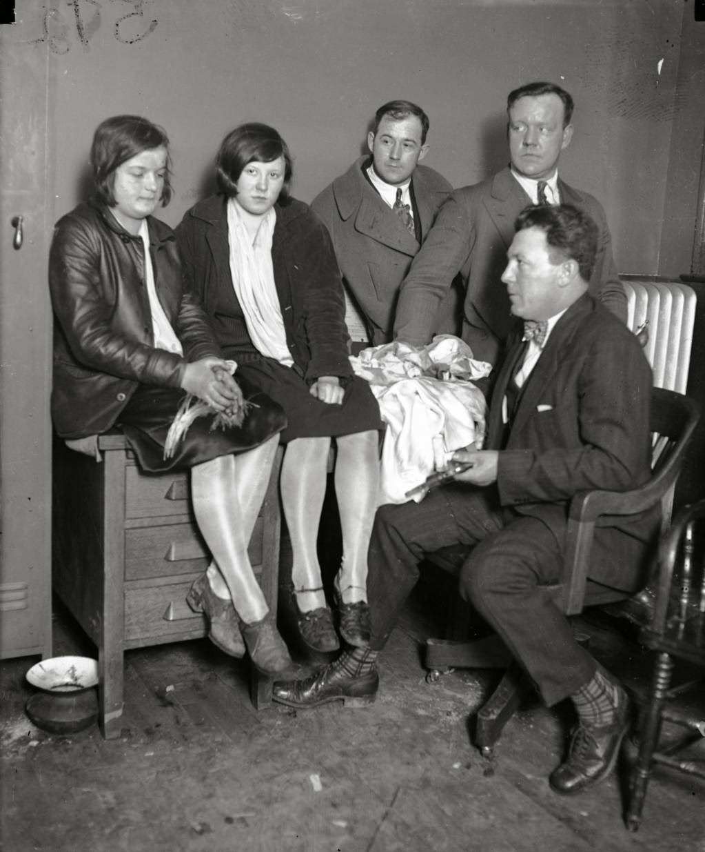 Girl bandits Jean Buttick, 15, and Anna Varich, 16, were caught red-handed looting a bungalow at 6152 S. California Avenue on March 20, 1927. The Chicago Tribune reported "In the kitchen, as they seized her [Anna] she spilled rings, bracelets, beaded bags, and what not from every part of her clothes. When they shook her she literally dripped booty." Police officers believe the two bandits had looted about a dozen other homes within two weeks time. With Buttick and Varich are Charles Goss, Bert Harlem and Sgt. William H. Doyle (in chair) on March 20, 1927.