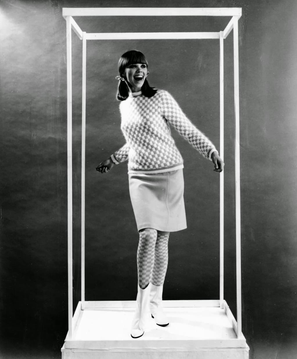 "Kicky checkerboard pattern of the crew necked pullover (about $16) banded with two-tone stripes at hips, cuffs and neck is echoed in the high socks. Welt seamed skirt (about $11) is an easy A line." And, of course, white go-go boots, another Mary Quant innovation. 1965. — handout