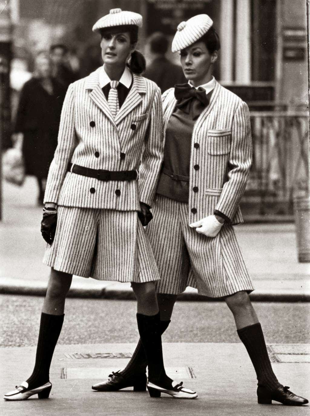 "Two London birds wear Christian Dior's striped suits, short and narrow, with emphasis on the hips. Suit at left is navy and white pin stripes, with navy blouse, pleated culottes, and horizontally striped tie. The cardigan version is in red and white stripes with scarlet socks and blouse." — UPI, May 12, 1966