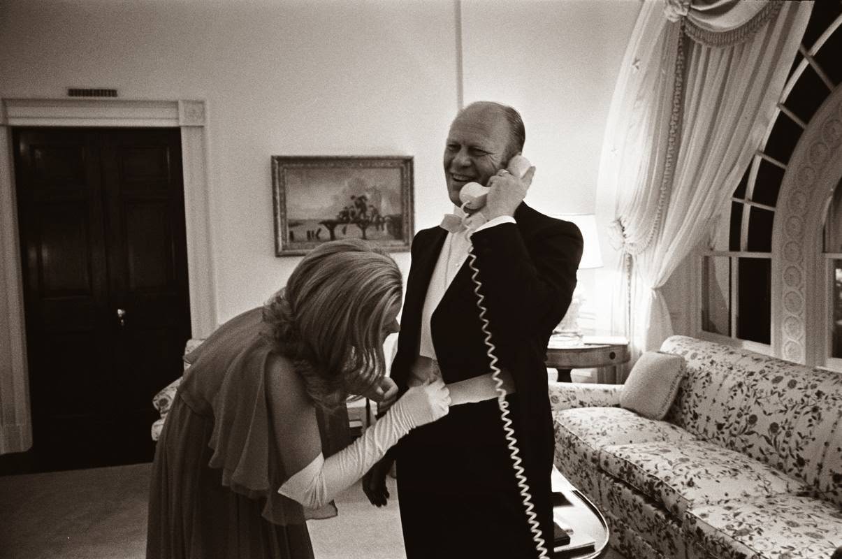 President Gerald R. Ford takes a phone call while his daughter Susan Ford adjusts her father's cummerbund before a white tie diplomatic reception in Washington, D.C., 1974.