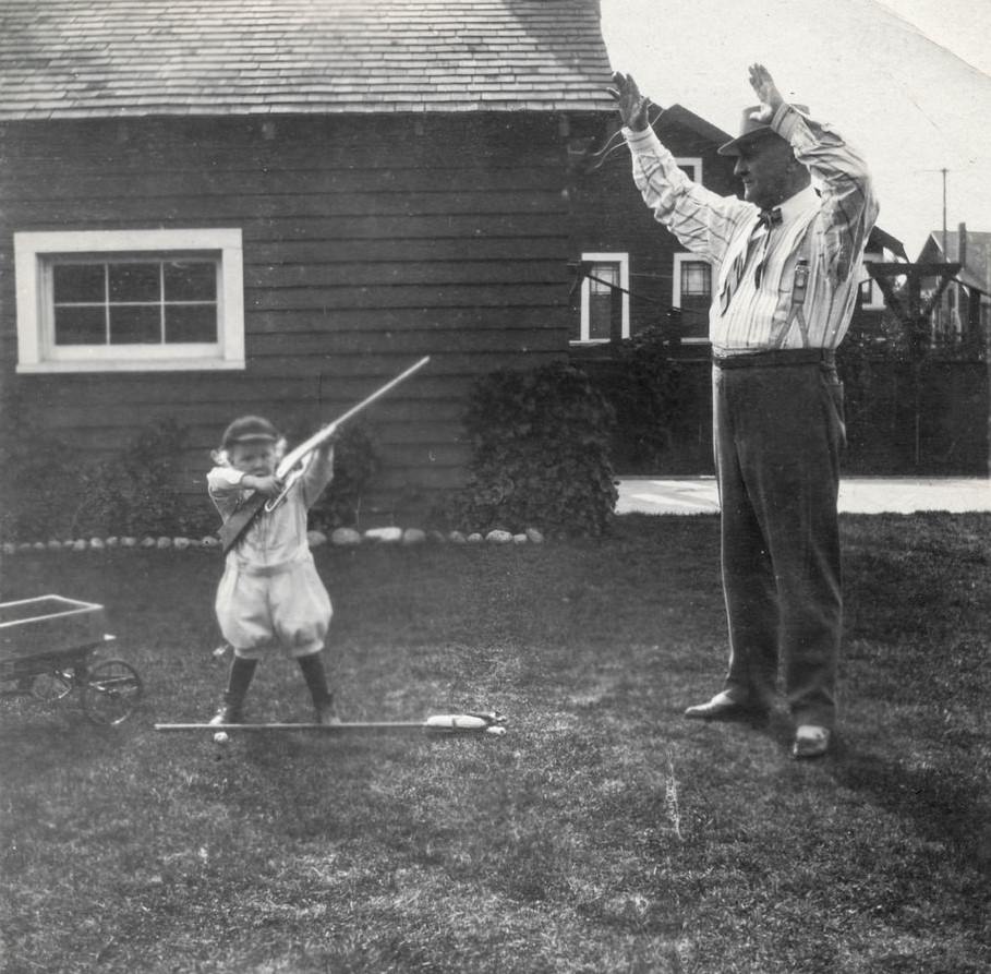 Little boy aims a rifle at his grandpa.