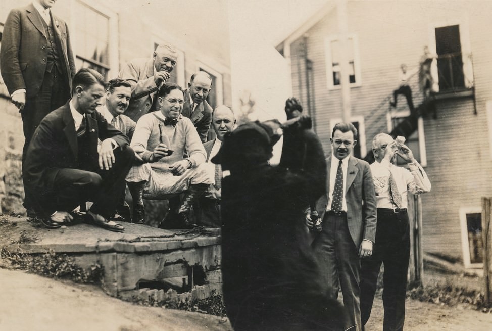 Men watching a bear drink from a bottle.